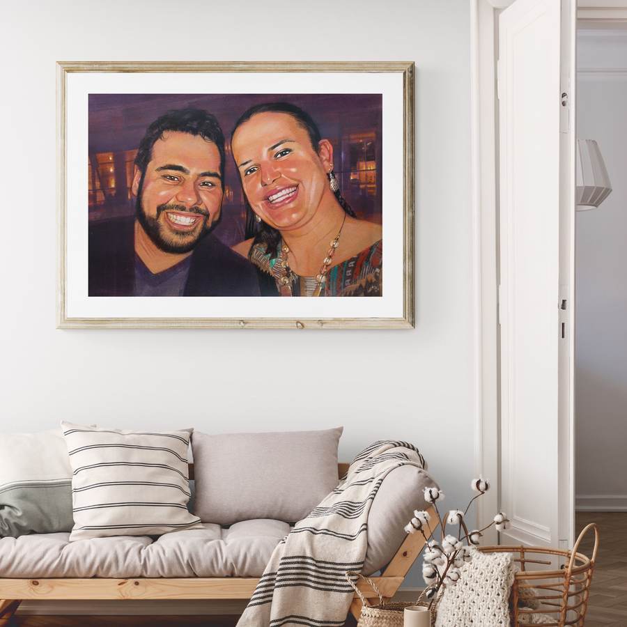 Retrato de casal emoldurado em madeira clara, acima de um sofá com almofadas.