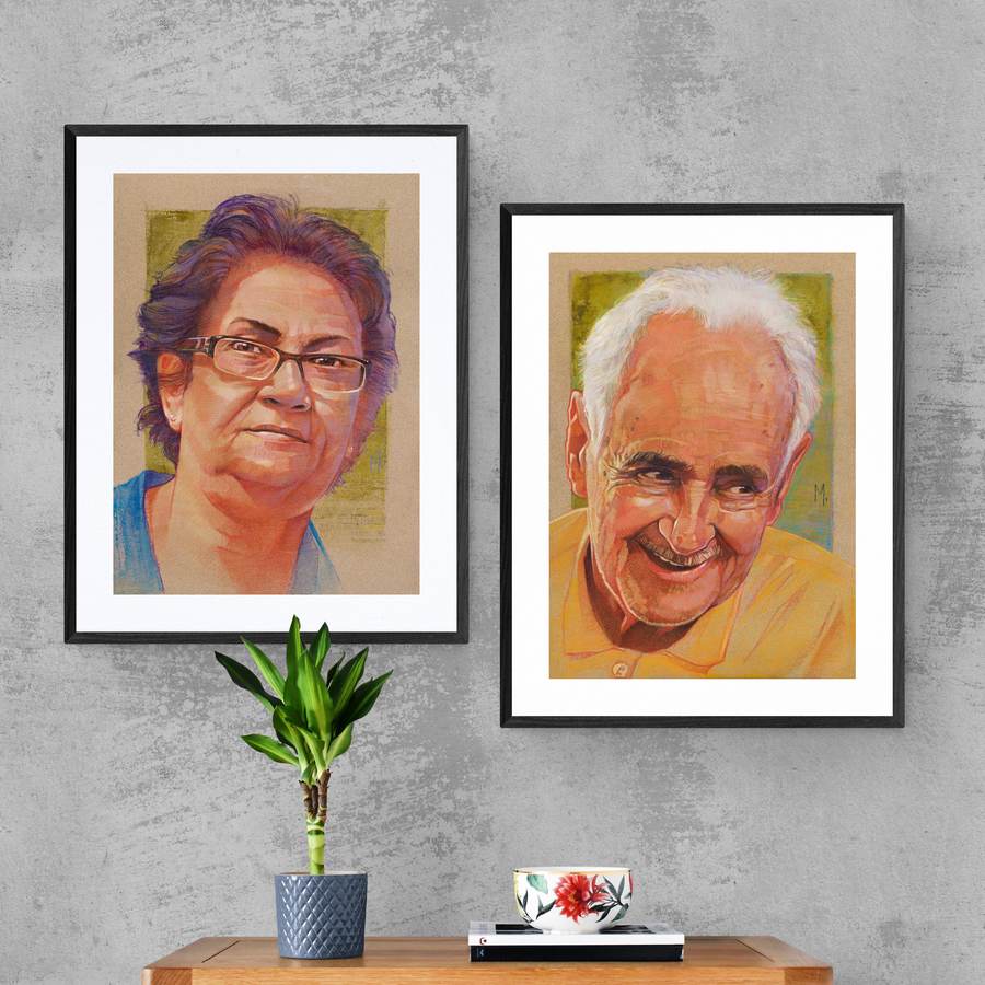 Dois retratos emoldurados lado a lado, acima de uma cômoda cinza com uma planta.